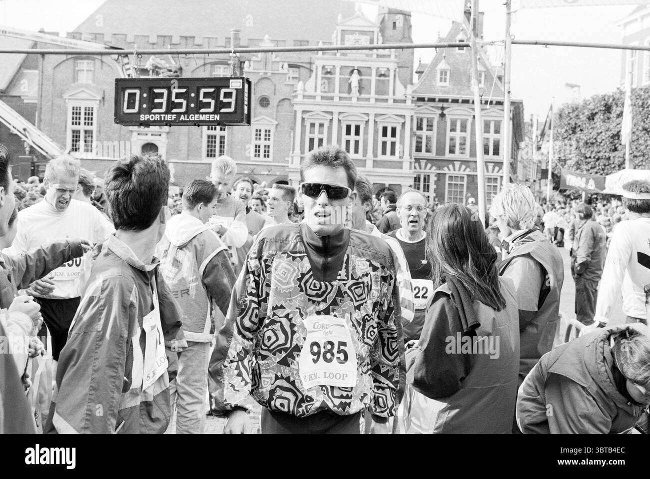 Trosloop 1992 partecipanti alla corsa di 8 chilometri attraversano il traguardo di Haarlem. Per gestire Haarlem Grote Markt Paesi Bassi, Whizgle News, Dutch Desk, Paesi Bassi, 1950 - 2000 il 18-10-1992. Questi sono gli elementi dell'immagine. La scena è piena di energia, mentre corridori e spettatori riempiono l'area dopo una gara. L'atmosfera e' carica di un mix di eccitazione ed esaurimento. In primo piano, un uomo che indossa una giacca dai motivi vivaci spicca tra la folla, la sua espressione riflette un mix di fatica e determinazione. I suoi occhiali da sole oversize aggiungono un tocco moderno, contrastando lo spirito Foto Stock