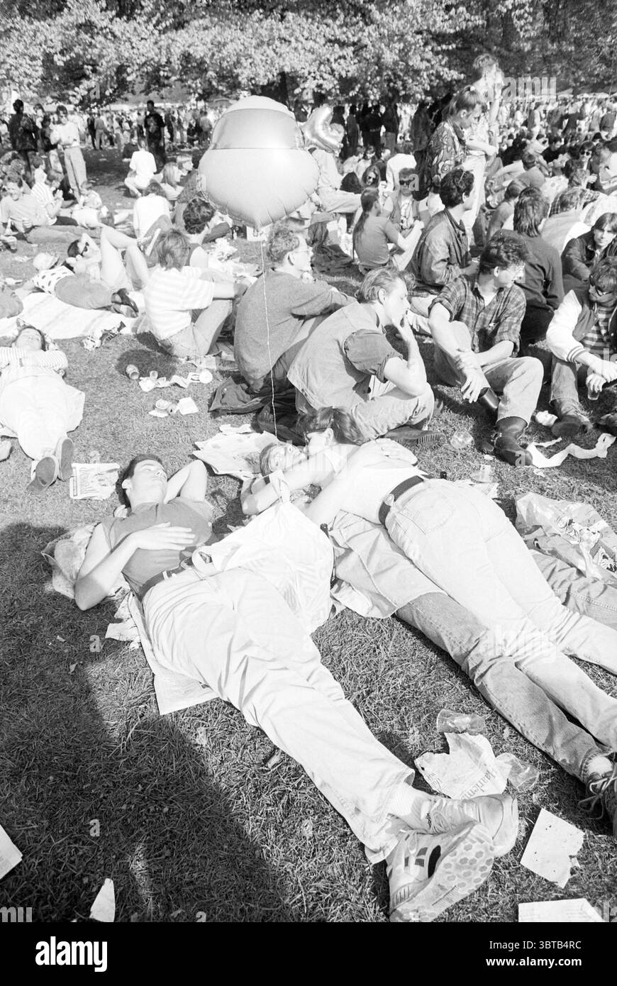 Haarlemmerhout Festival, Whizgle News, Dutch Desk, Paesi Bassi, 1950 - 2000 il 04-05-1992. Questi argomenti vengono visualizzati nell'immagine. La scena cattura un vivace raduno all'aperto, mostrando una folla vibrante e variegata sparsa in un'area erbosa. Gli individui sono sdraiati per terra, alcuni si rilassano comodamente mentre altri si siedono, sono impegnati in una conversazione o in un relax. Gli stili di abbigliamento sono vari, riflettendo un mix di tendenze casual e forse retrò, con molti outfit leggeri e poco aderenti che parlano di un'atmosfera estiva spensierata. Alcuni corpi sono intrecciati, suggerendo intimità e cameratismo Foto Stock