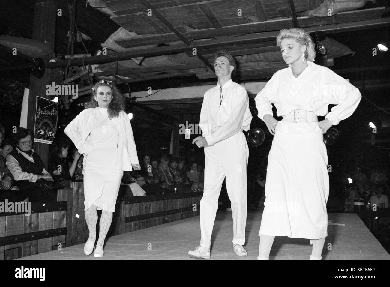 Sfilata di moda in Claus Party House Fashion, Whizgle News, Dutch Desk, Paesi Bassi, 1950 - 2000 il 27-03-1986. Questi argomenti sono mostrati nell'immagine. La scena cattura una vivace sfilata di moda ambientata in un locale al coperto con un fascino rustico. La pista è ben visibile al centro, illuminata da un'illuminazione soffusa che diffonde una calda luce soffusa. L'atmosfera sembra energica e leggermente nostalgica, suggerendo un'epoca passata. Tre modelli sono al centro della scena, ciascuno vestito con abiti bianchi. La prima modella, a sinistra, è caratterizzata da un'espressione audace e i suoi capelli sono stati ridisegnati in modo spettacolare. Lei lo sho Foto Stock