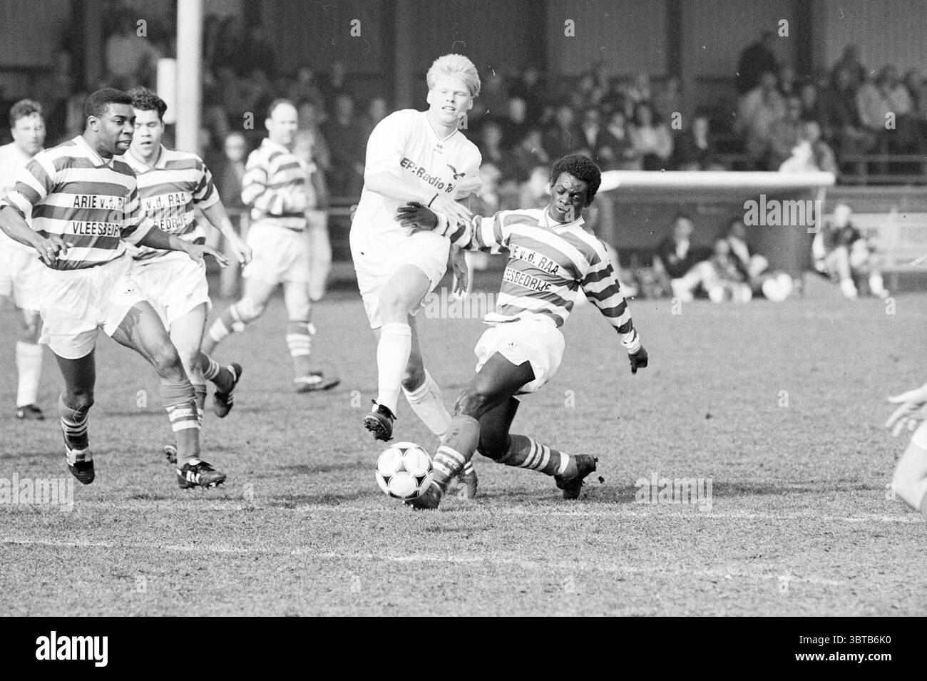 Storm-petrels - Blue-White, Whizgle News, Dutch Desk, Paesi Bassi, 1950 - 2000 il 11-03-1995. Questi argomenti sono mostrati nell'immagine. La scena cattura un momento dinamico su un campo da calcio erboso, dove è evidente uno scontro di atletismo. In primo piano, due giocatori sono in movimento. Uno, indossando una maglia a righe nelle tonalità del verde e del bianco, è capace di manovrare con determinazione la palla. L'altro, vestito con una uniforme bianca, sembra tentare un gioco difensivo, mostrando un'espressione concentrata mentre si allontana in avanti. Intorno a loro, l'atmosfera è piena di energia. Altro gioco Foto Stock