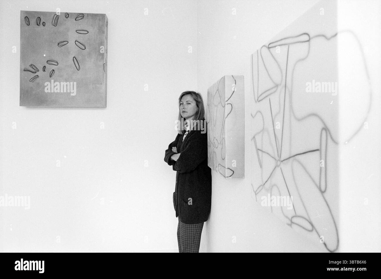 Louise de Haan nuova. Gallery H'lem Haarlem Paesi Bassi, Whizgle News, Dutch Desk, Paesi Bassi, 1950 - 2000 il 08-09-1996. Questi argomenti sono mostrati nell'immagine. In uno spazio minimalista e pieno di arte, una donna si trova contro un muro bianco, trasudando un comportamento contemplativo. È vestita con un blazer scuro, le sue linee sartoriali contrastano con la natura casual della sua postura: Braccia incrociate, un leggero solco nella fronte che suggerisce un pensiero profondo. Alla sua sinistra, un'opera d'arte testurizzata composta da forme organiche ovali in una tavolozza di grigio tenue attira l'attenzione. La sua superficie liscia contrasta con la surr Foto Stock