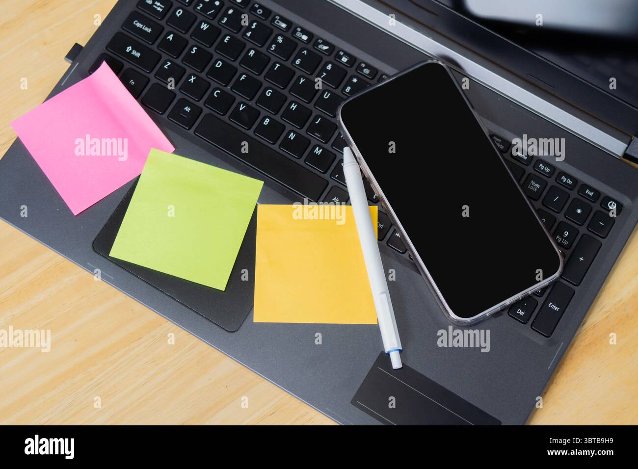 Tavolo da ufficio in legno con penna, carta per appunti e smartphone sul computer portatile. Vista dall'alto, copia spazio. Foto Stock