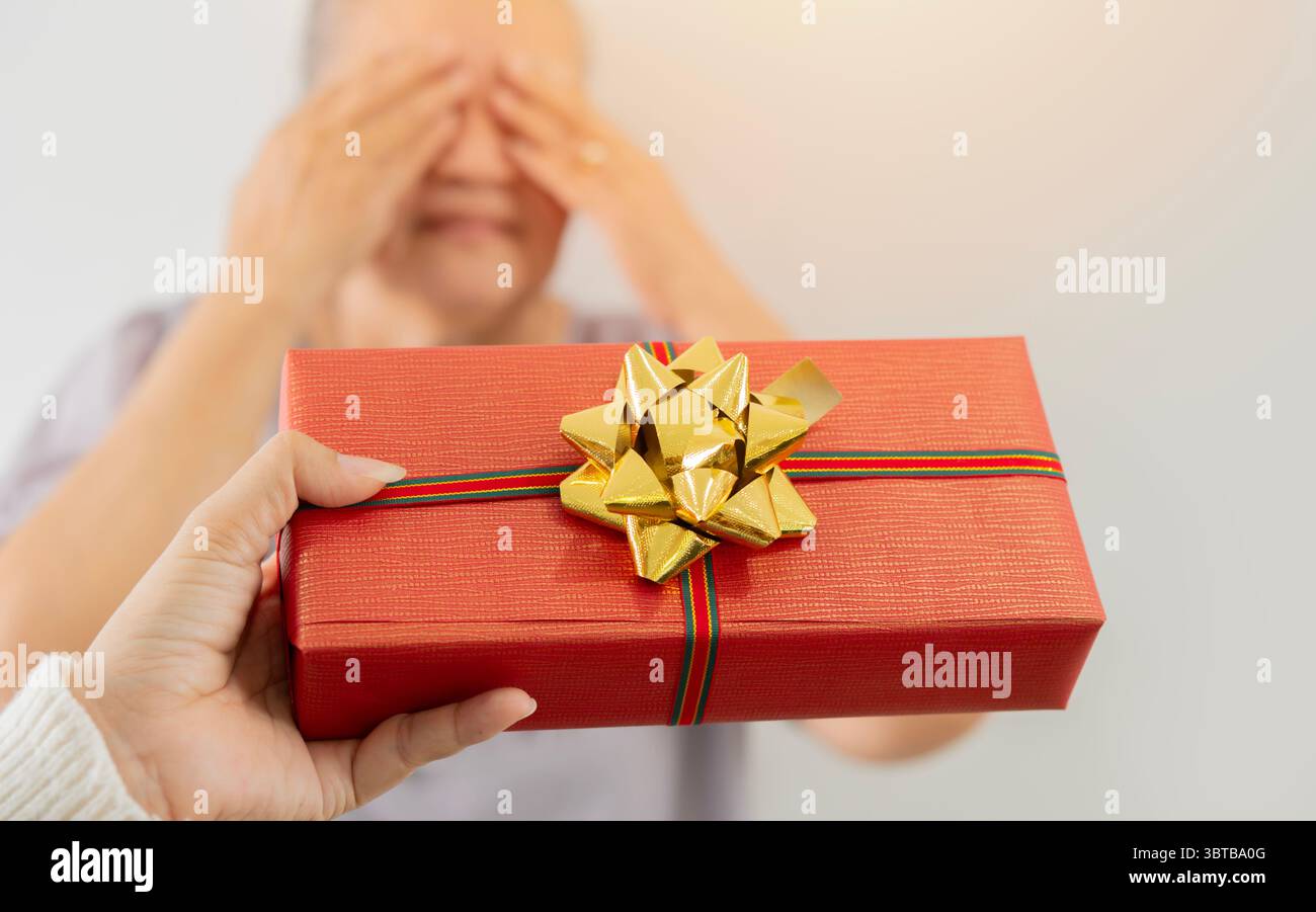 Primo piano di una scatola regalo rossa di natale tenuta per mano della figlia per una sorpresa da regalare alla sua anziana madre. Concetto di offerta a sorpresa. Foto Stock