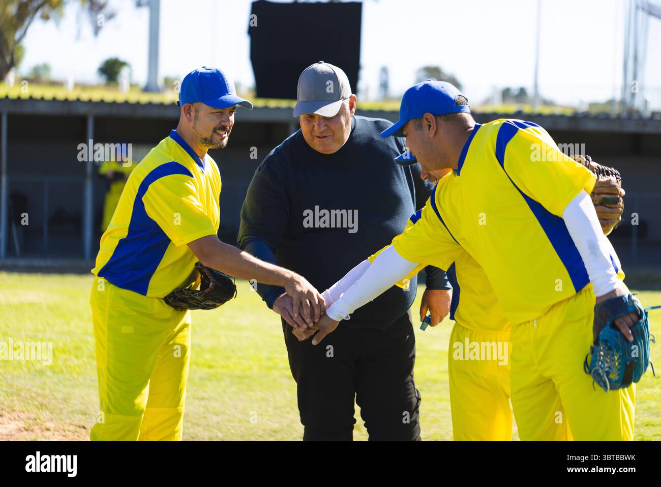 Allenatore di baseball e giocatori maschili si accoccolano prima di iniziare la partita sul campo di erba con i guanti Foto Stock