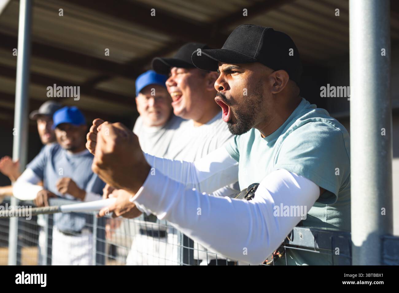 Diversi compagni di squadra maschi indossano maglie e berretti che tifanno e tengono sotto il braccio il guanto in dugout Foto Stock