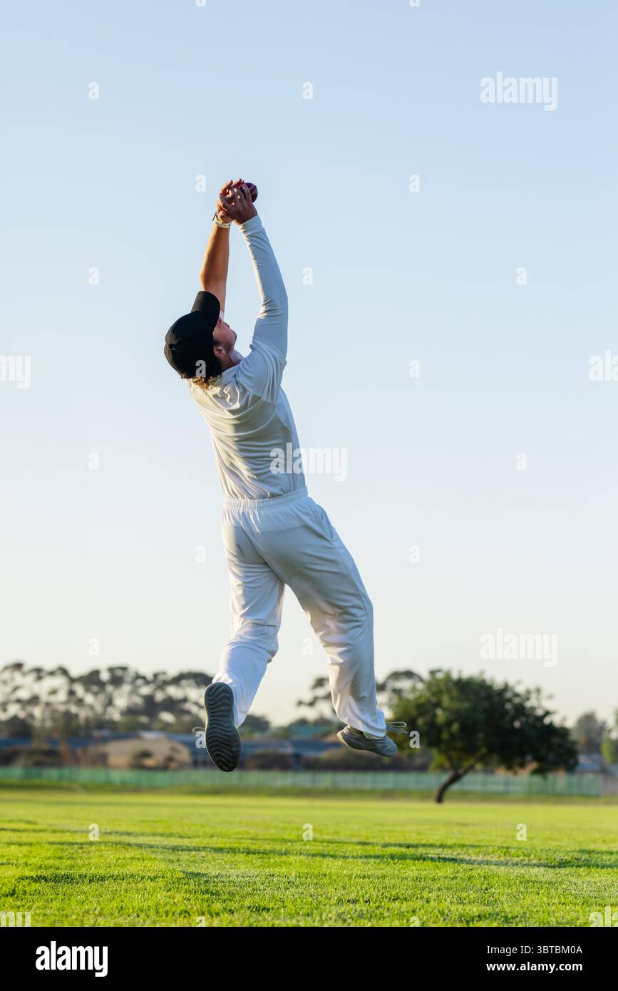 Uomo indiano che salta e cattura palla di cricket rossa su un campo erboso sotto il cielo azzurro Foto Stock