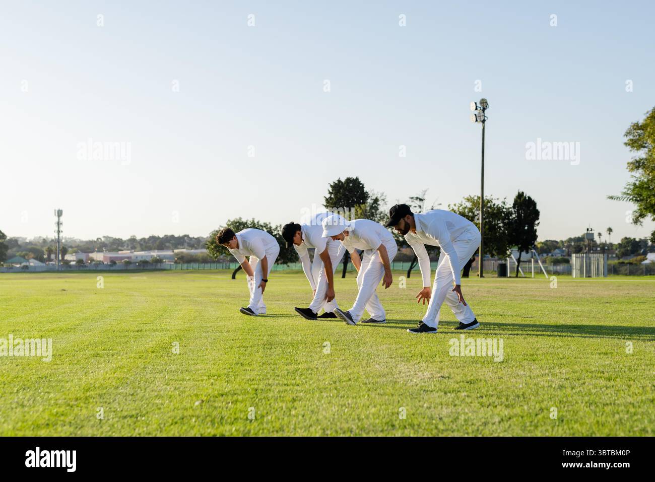 Diversi giocatori maschili di cricket che si piegano in avanti e si allungano all'esterno indossando uniformi e cappelli Foto Stock