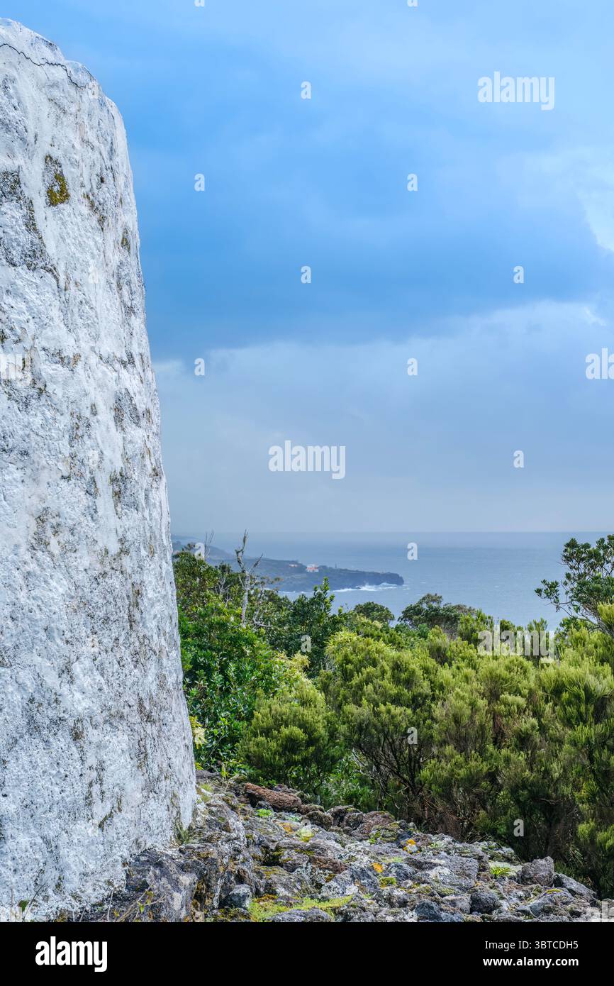 Mulino a vento sulle Azzorre dell'isola di Sao Jorge con vista sull'oceano Atlantico. Scogliere calcaree bianche, vegetazione verde lussureggiante, paesaggio dell'isola portoghese Foto Stock