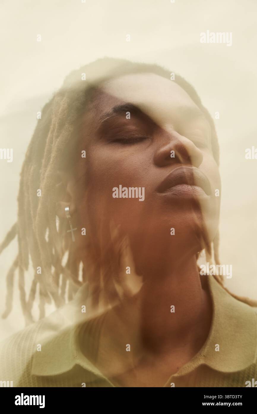 Giovane adulto, uomo Nero che chiude gli occhi con la testa leggermente inclinata, con orecchini, dreadlock di media lunghezza visibili, effetto di messa a fuoco morbido che crea un'impressione visiva a doppia esposizione Foto Stock