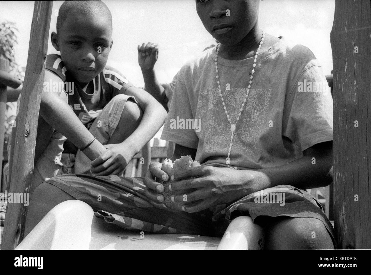 14 maggio 2014, Pietermaritzburg, KwaZulu Natal, Sud Africa: Due ragazzi mangiano un panino secco sulla cima di uno scivolo in un'area giochi in disuso ai margini dell'insediamento informale Jika Joe...Jika Joe è un insediamento informale che si trova a cavallo di entrambe le rive del fiume Dorpspruit nel centro di Pietermaritzburg, la capitale della provincia di KwaZulu Natal in Sud Africa. La sua massa è fatta di fango, frammenti di legno e cartone, i tetti di Jika Joe sono in lamiera, pezzi di pannelli rigidi e teloni venduti spazzati via dai camion di passaggio su una vicina autostrada. . La vista di queste case autocostruite su tratti aperti di Foto Stock