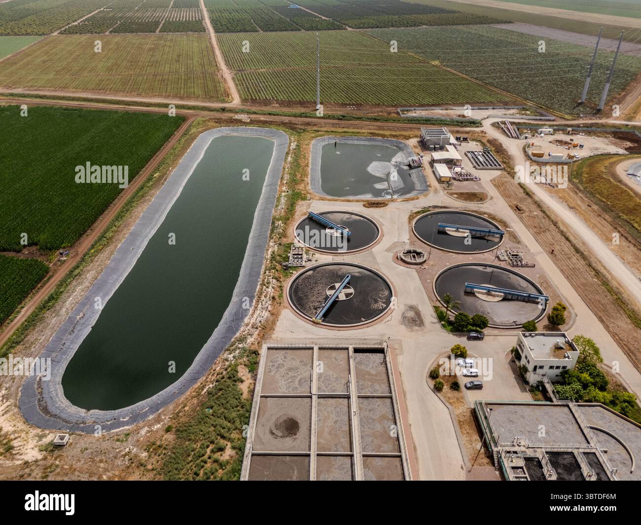 Vista aerea dell'impianto di trattamento delle acque circondato da campi agricoli, contrastando l'acqua scura con le colture verdi, Kfar Masaryk, North District, Israele. Foto Stock