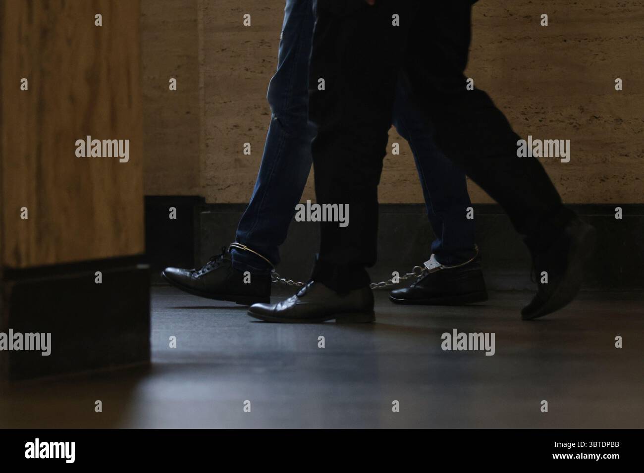 Un uomo arrestato con le manette alle gambe viene scortato in tribunale. Foto illustrativa. Foto Stock