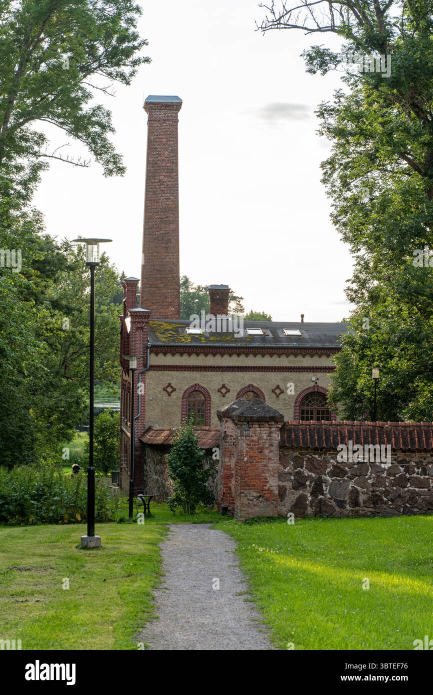 Edificio della distilleria Mooste in Estonia visto da dietro, con alto camino in mattoni, finestre ad arco e vegetazione naturale - architettura storica Foto Stock