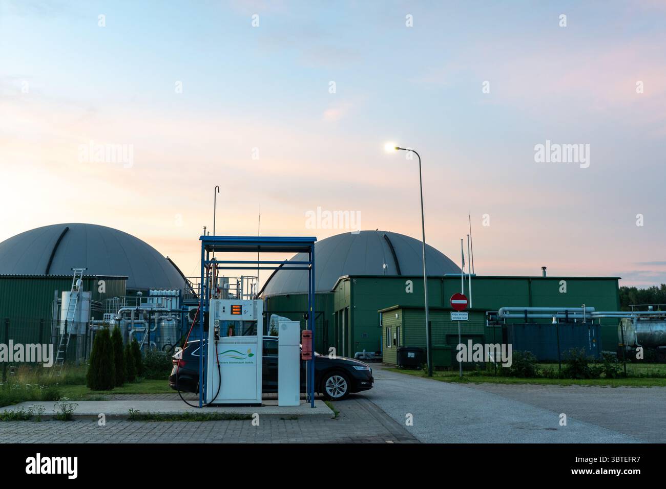 Stazione di rifornimento di biogas in Estonia con digestori a forma di cupola sullo sfondo, illuminati dalla luce soffusa della sera, un tranquillo incrocio di fonti rinnovabili Foto Stock