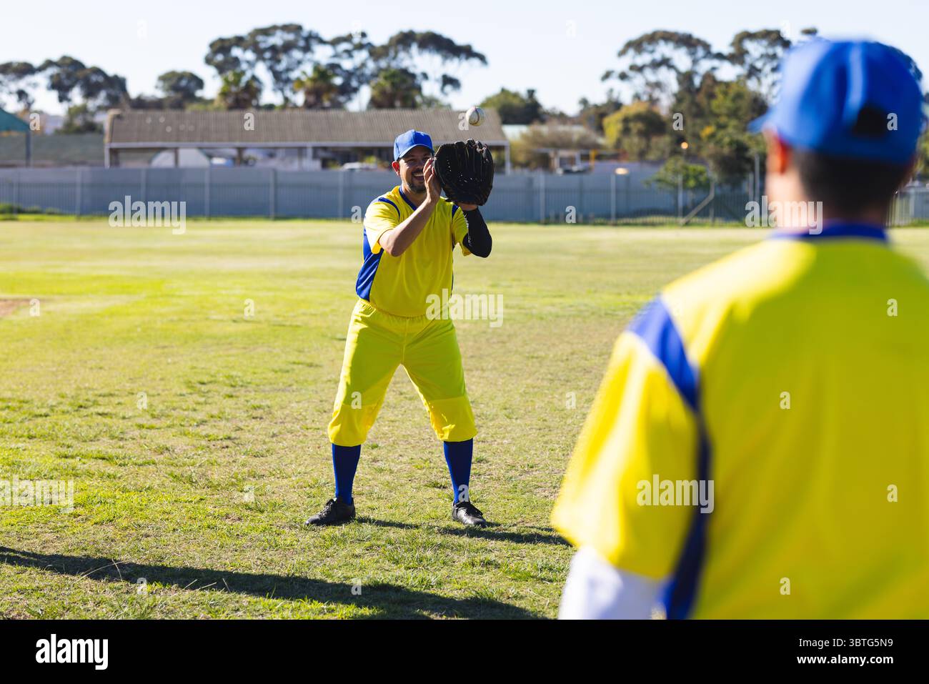 Diversi compagni di squadra maschi che praticano la cattura del baseball sul campo con uniformi gialle-blu con guanti Foto Stock