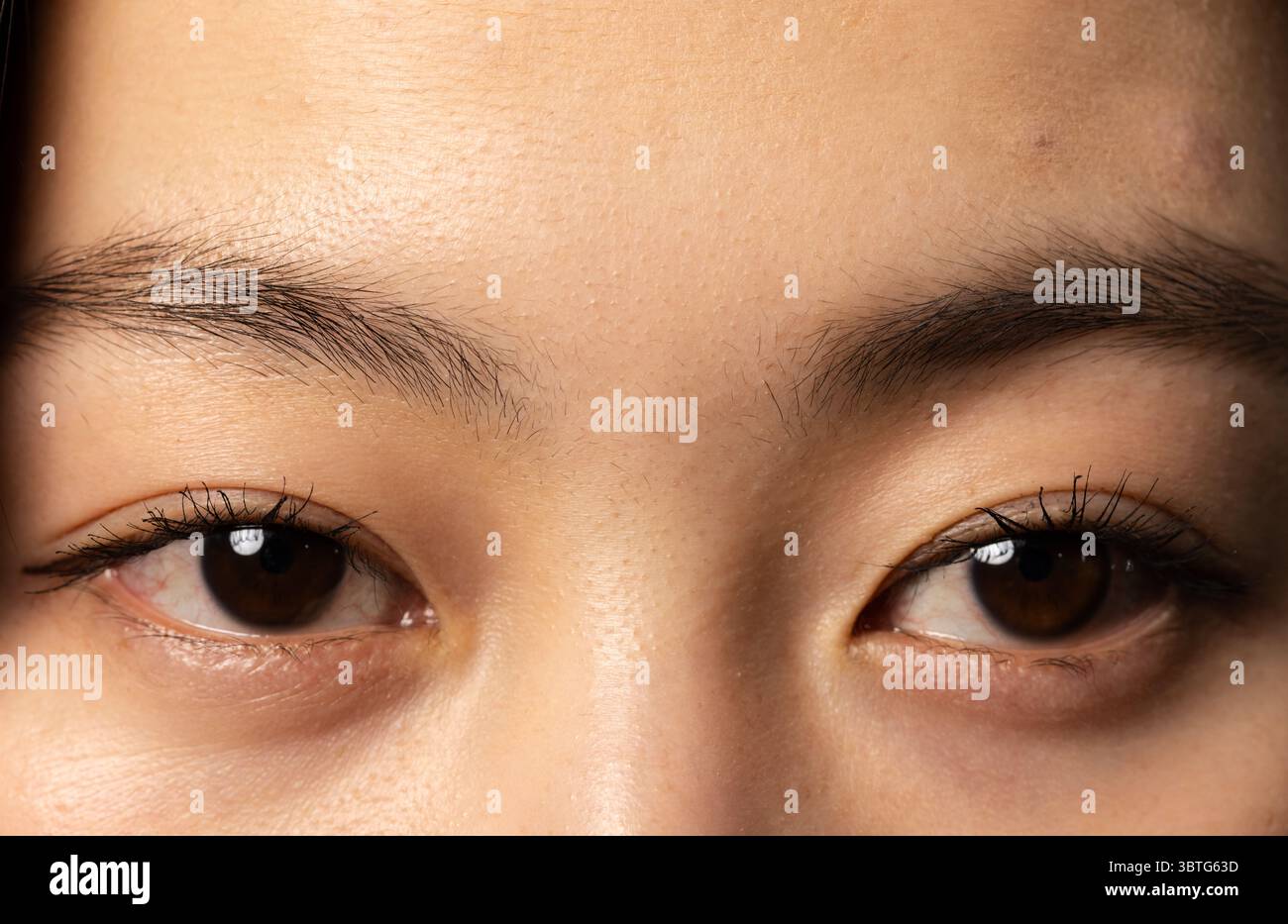 Donna cinese asiatica che mostra una texture liscia della pelle degli occhi sotto una luce soffusa da studio Foto Stock