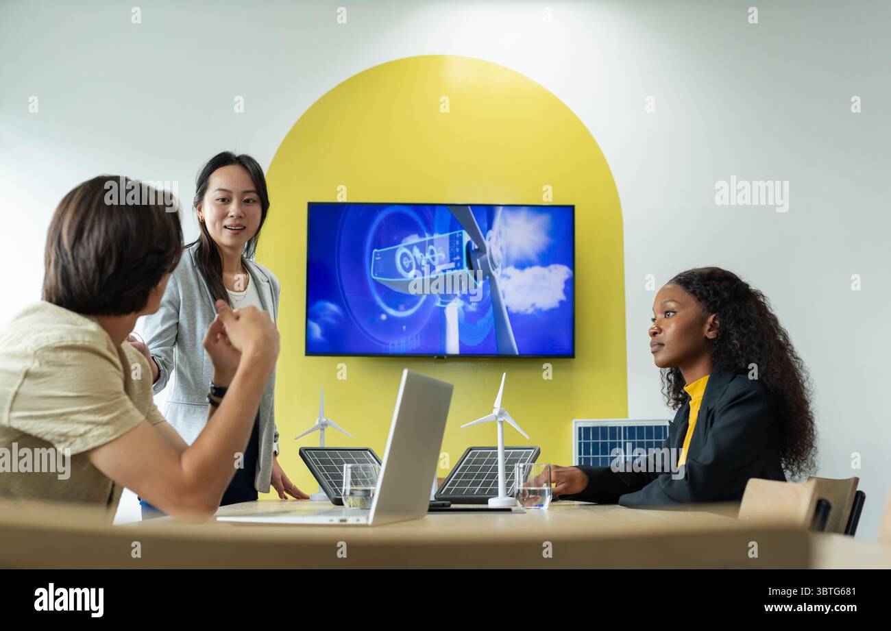 Colleghi diversi che discutono di energia rinnovabile al tavolo delle conferenze con computer portatili e modelli di turbine Foto Stock