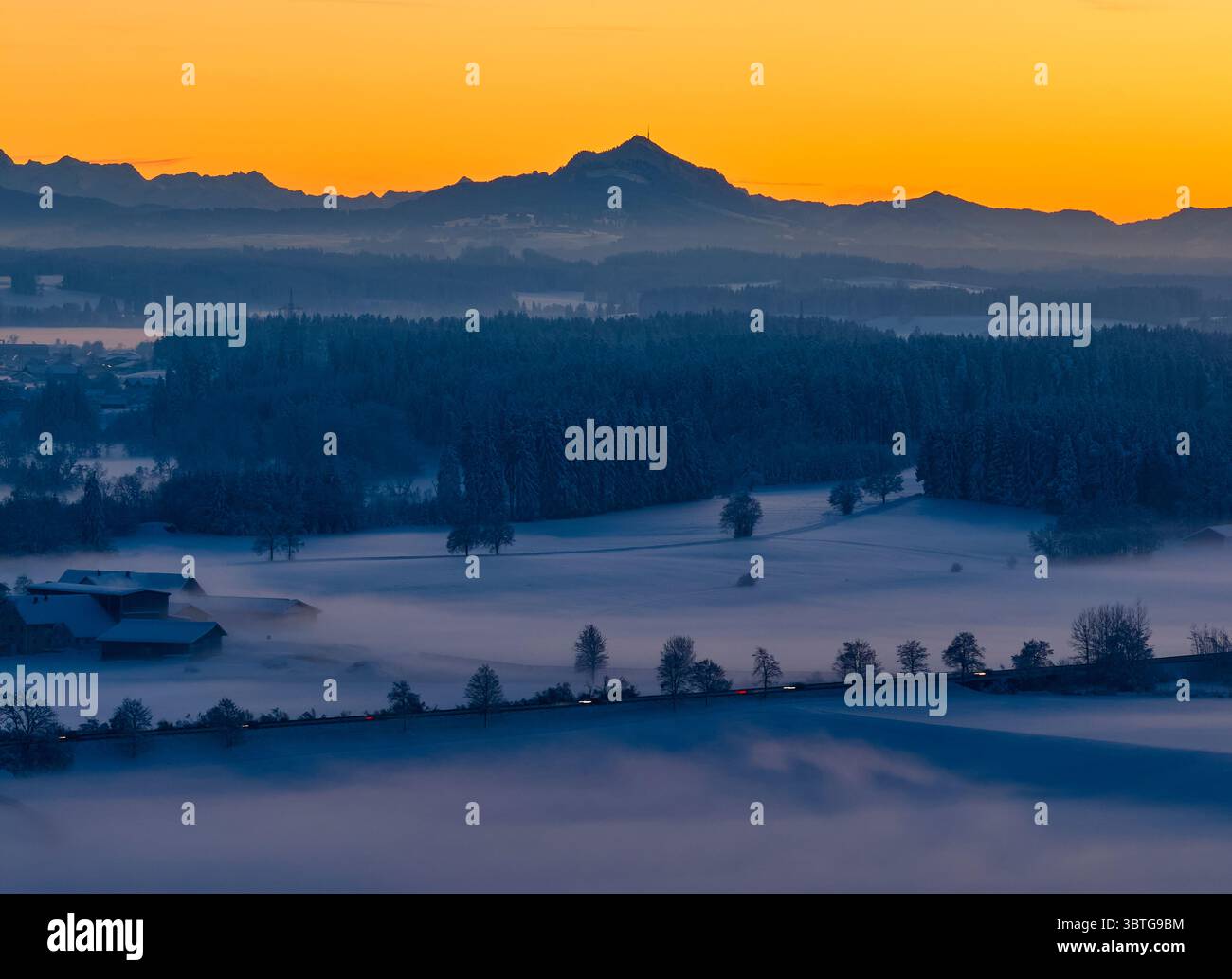 Veduta aerea dell'alba dorata che baciava le Alpi, con la nebbia che rotola dolcemente sui campi di Marktoberdorf, Bayern, Germania. Foto Stock