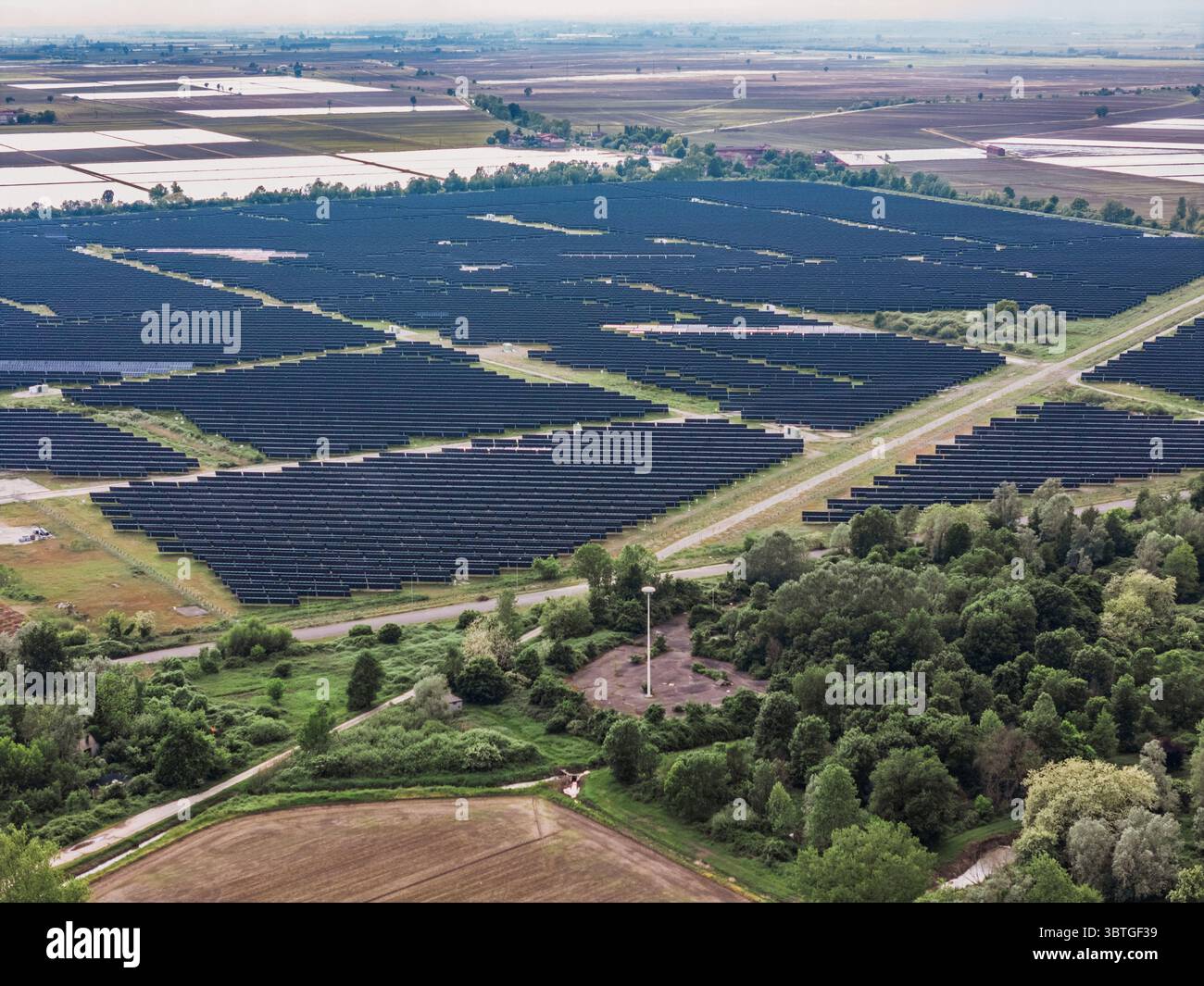 Veduta aerea di un'estesa fattoria solare, una griglia scura in contrasto con il verde circostante e i campi lontani, Trino, Piemonte, Italia. Foto Stock