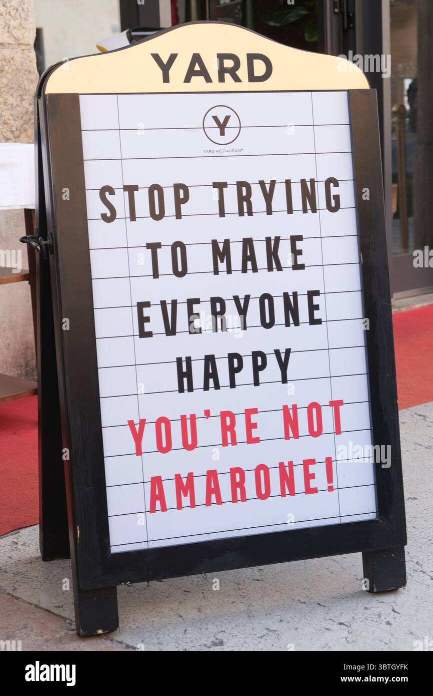 Un cartello con la linguetta fuori da un'enoteca di Verona avverte DI SMETTERE DI CERCARE DI RENDERE TUTTI FELICI. NON SEI AMARONE Foto Stock