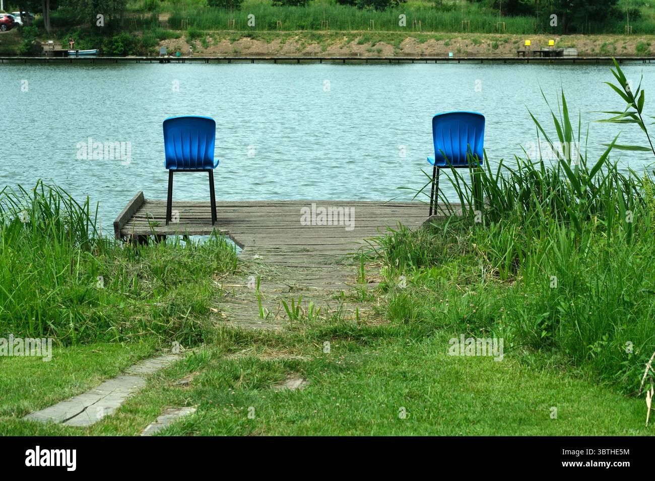 Due sedie blu siedono su una banchina di legno che si affaccia su un lago naturale. Foto Stock