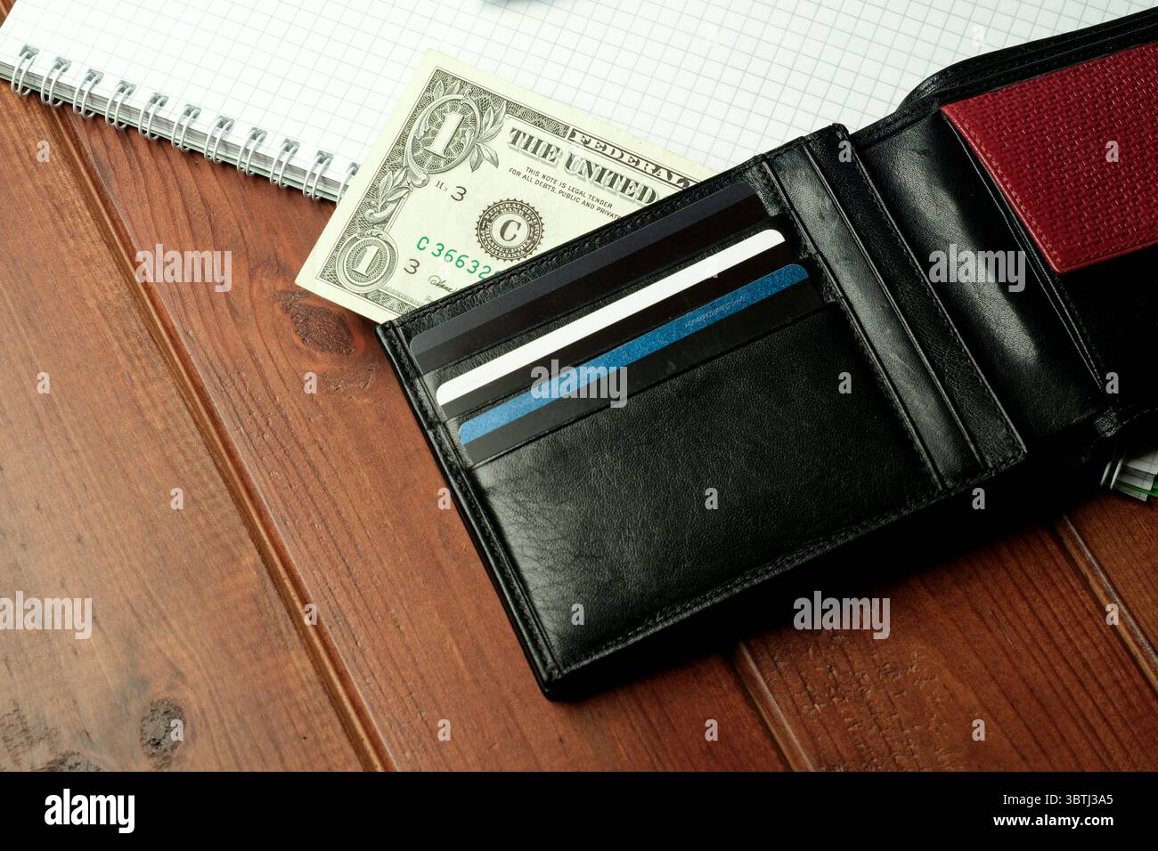 Un elegante portafoglio nero si appoggia su un tavolo in legno e contiene contanti e carte. Foto Stock