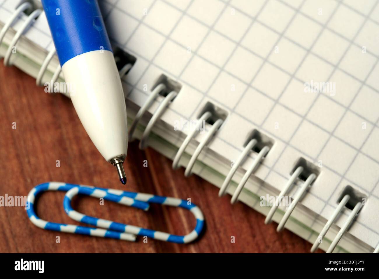 Una penna blu si trova accanto a un quaderno a griglia e a una graffetta che suggerisce ispirazione. Foto Stock