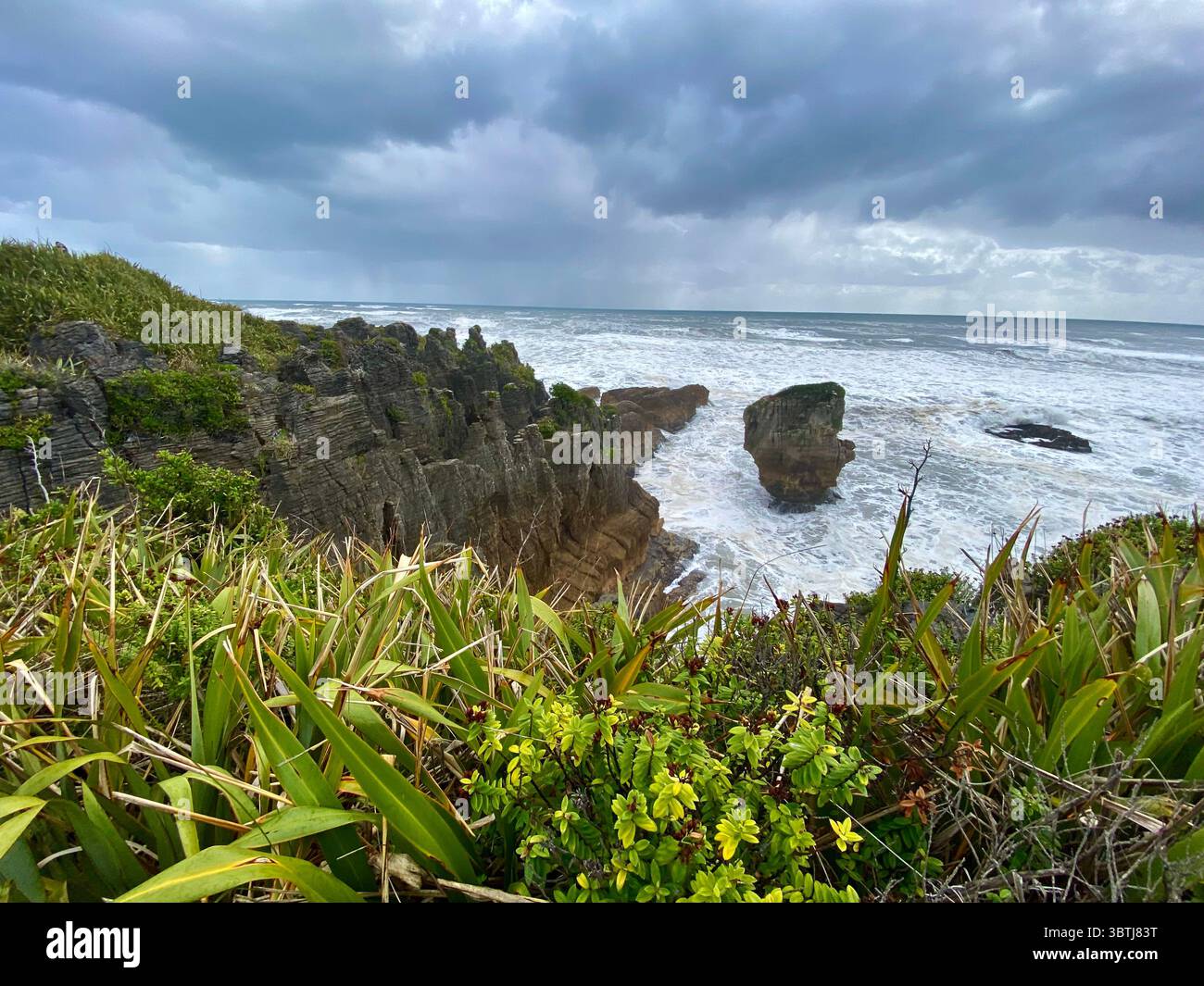 Vista panoramica della costa di Pancake Rocks in nuova Zelanda, con formazioni calcaree a strati, spiaggia sabbiosa, colline verdi e oceano calmo Foto Stock