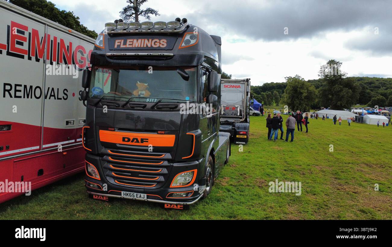 Vista aerea di una fila di veicoli industriali lucidati, compresi i modelli Scania, Volvo e DAF, parcheggiati su un campo erboso durante una fiera dei veicoli in Scozia Foto Stock