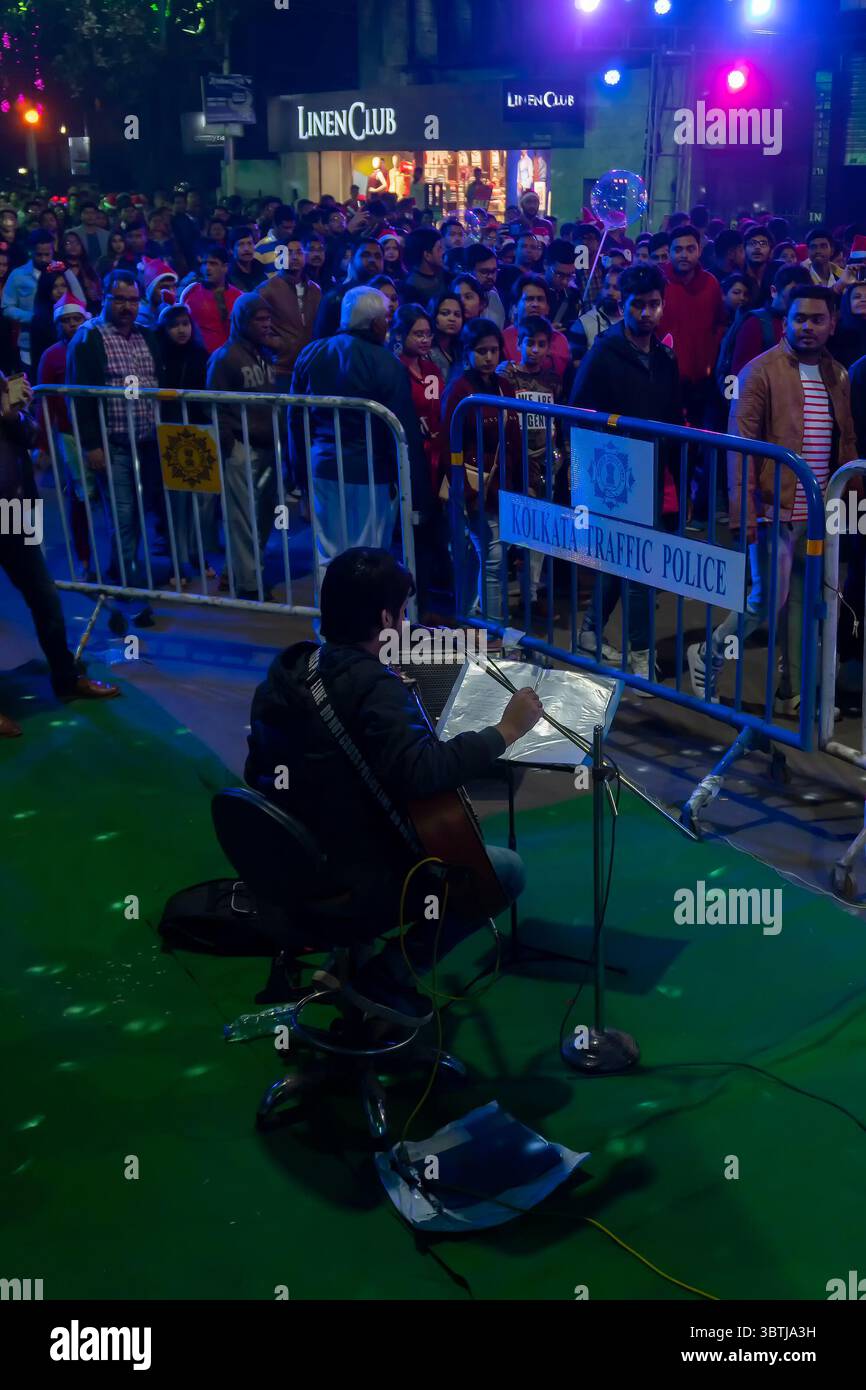 Kolkata, Bengala Occidentale, India - 25.12.2018 : cantante di strada che canta canzoni natalizie mentre i giovani si divertono a Park Street illuminata. Foto Stock