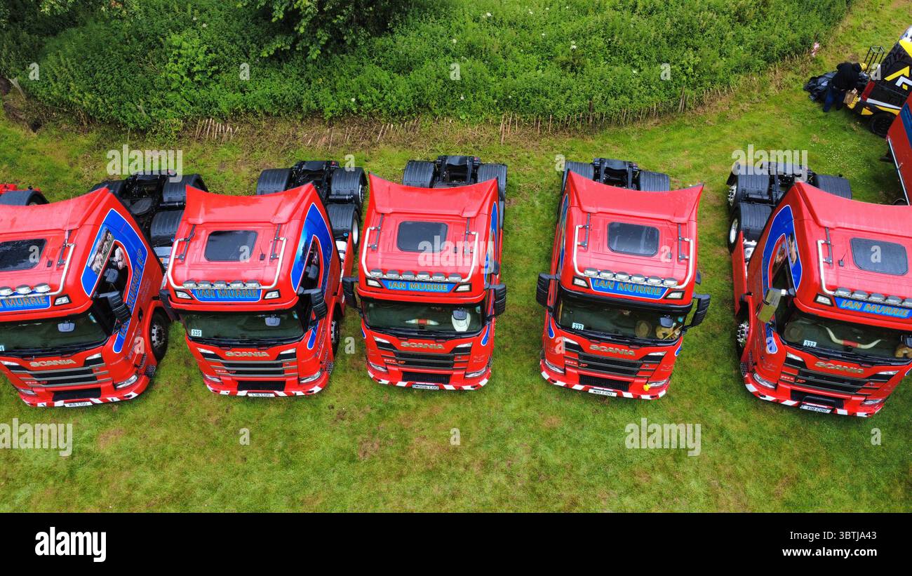 Vista aerea di una fila di veicoli industriali lucidati, compresi i modelli Scania, Volvo e DAF, parcheggiati su un campo erboso durante una fiera dei veicoli in Scozia Foto Stock