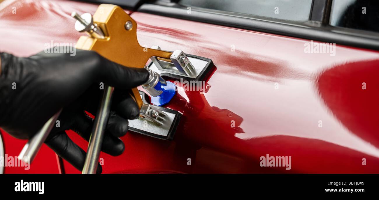attrezzo di riparazione ammaccature per auto senza verniciatura. Uomo che fissa la portiera del veicolo danneggiata con tecnologia PDR Foto Stock