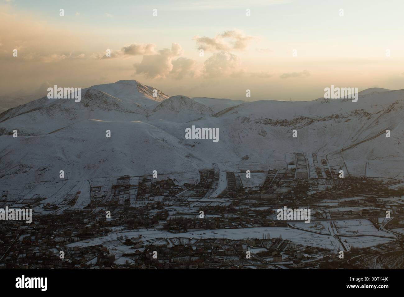 Vista aerea della città di Damavand in Iran coperta di neve, catturata alla luce del tramonto nel freddo inverno del 2024. Foto Stock