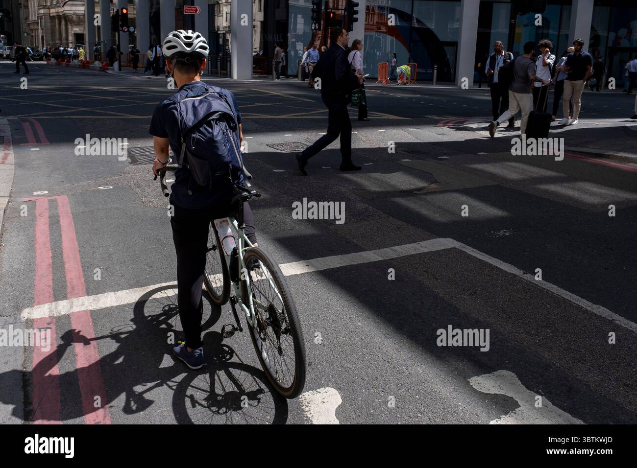 Ciclista che indossa un casco da bici in attesa al semaforo della City di Londra l'8 luglio 2025 a Londra, Regno Unito. La bicicletta è un mezzo di trasporto molto popolare nella capitale, poiché le persone cercano di evitare i trasporti pubblici, risparmiando denaro, allenandosi e risparmiando tempo. Foto Stock
