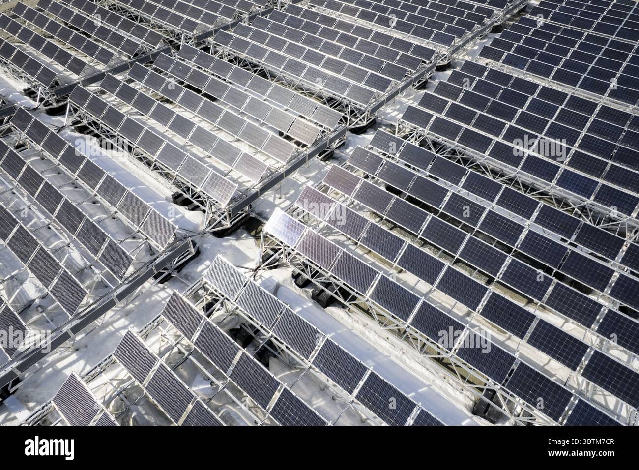 Vista aerea di file di pannelli solari che si estendono attraverso il paesaggio, riflettendo la luce del sole con una lucentezza metallica, creando un netto contrasto con il terreno pallido, posizione omessa, posizione omessa. Foto Stock