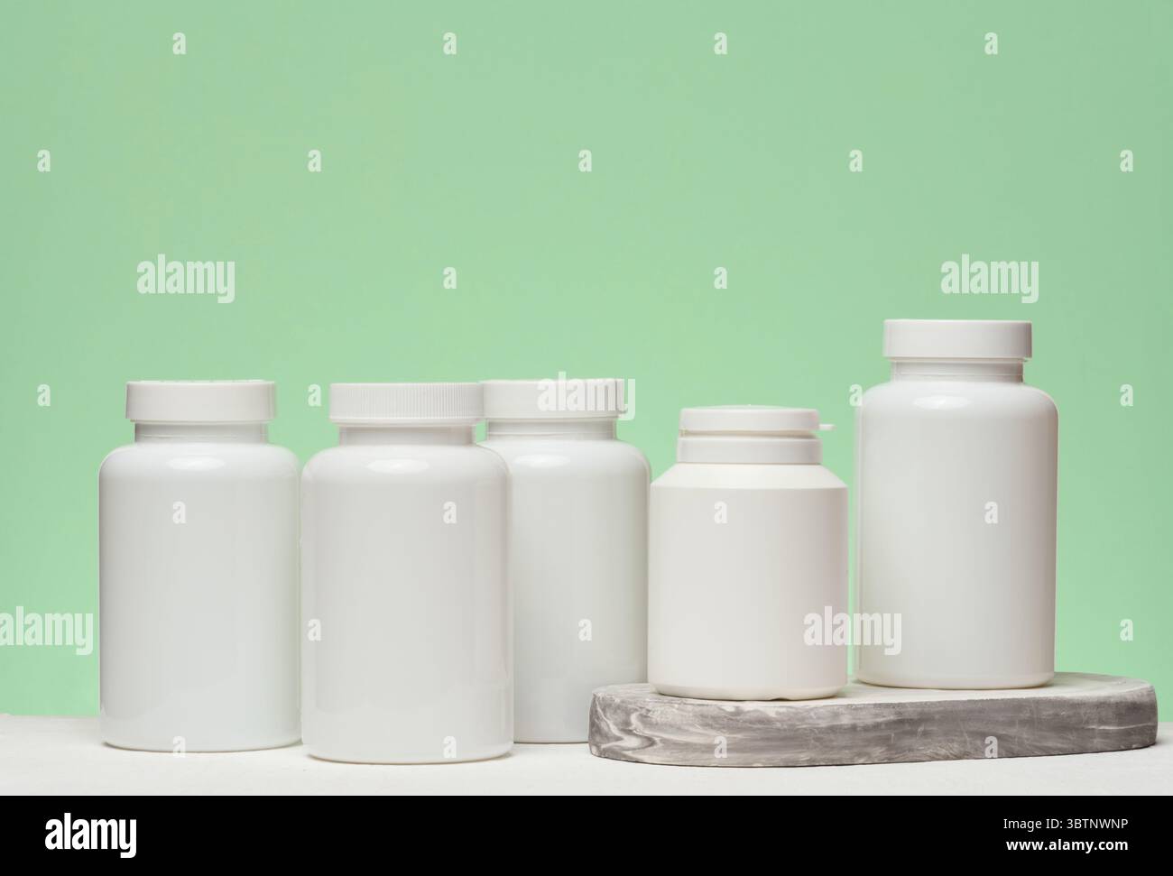 Diversi vasetti di plastica bianchi con pillole su sfondo verde. Articoli relativi alla medicina e all'assistenza sanitaria Foto Stock