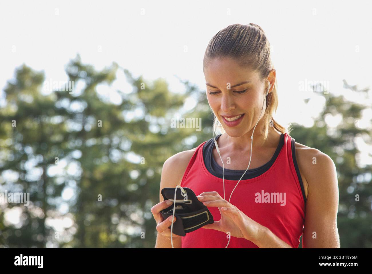 Donna bionda con cuffie che guardano verso il basso lo smartphone Foto Stock
