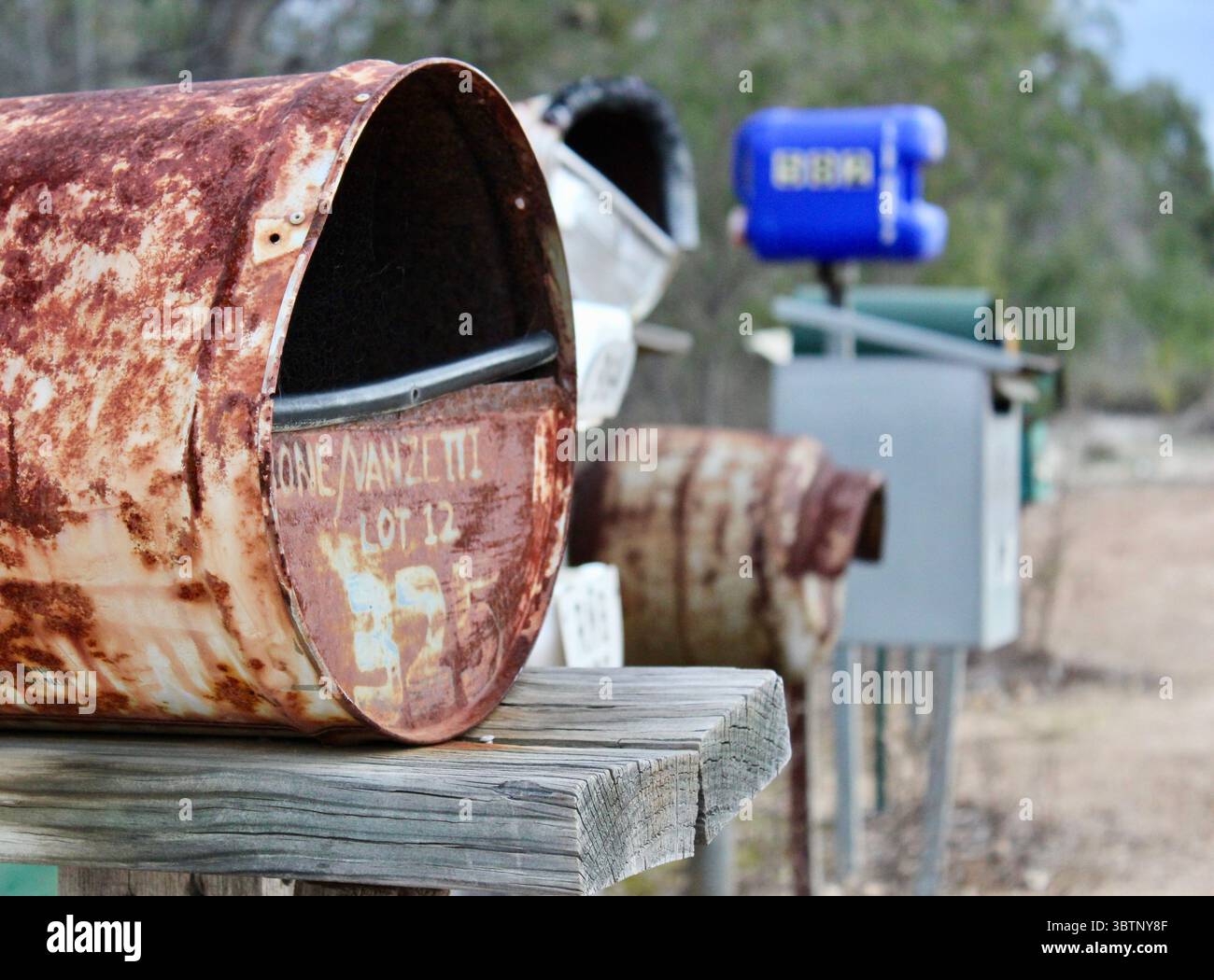 Cassetta postale in metallo rusty e fila di cassette postali rurali lungo la polverosa Outback Road, Australia Foto Stock
