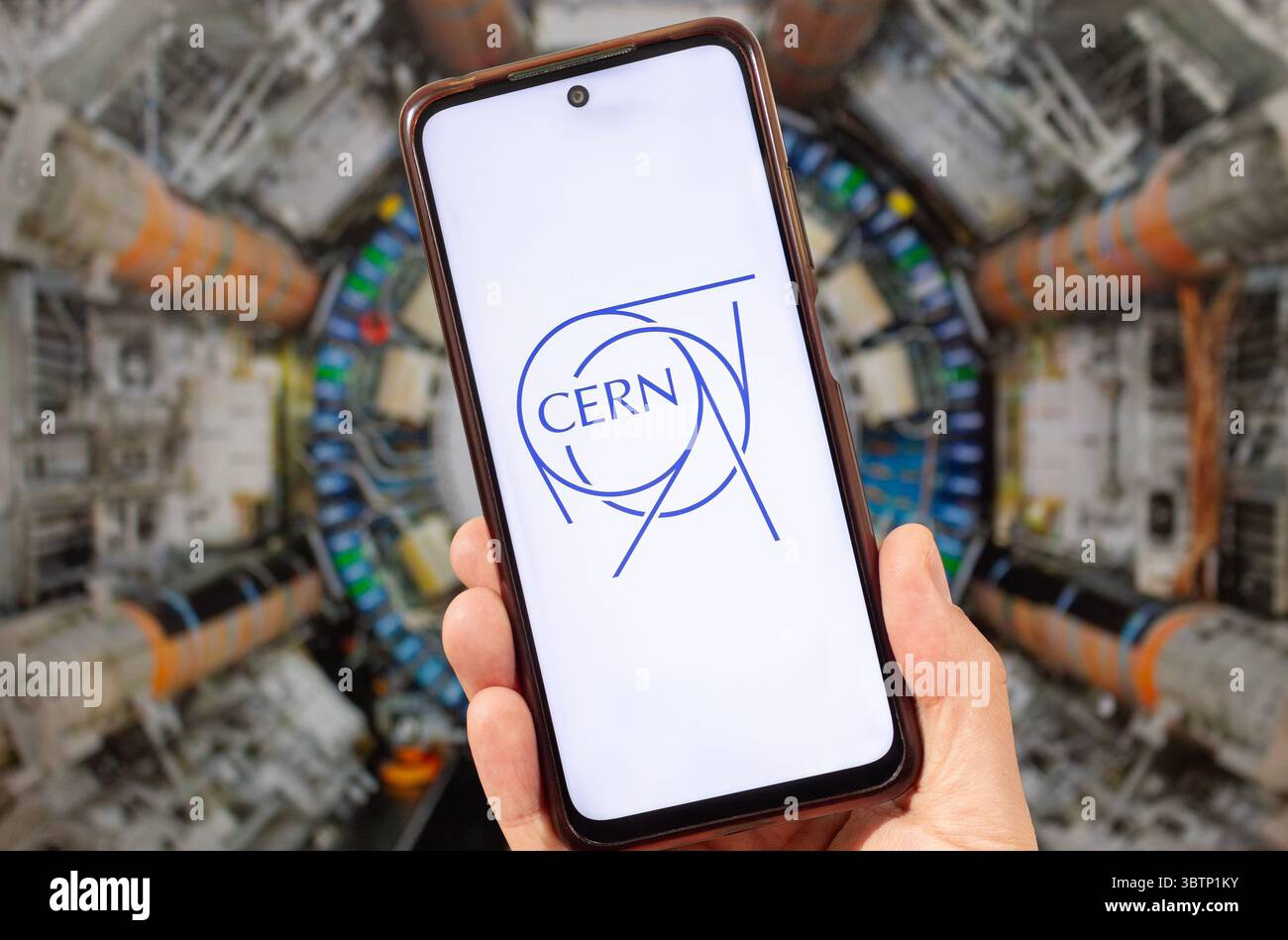 BOGOTÀ, COLOMBIA - 14 LUGLIO 2025 una mano maschile che tiene uno smartphone con il logo del CERN e sullo sfondo un Large Hadron Collider sfocato Foto Stock