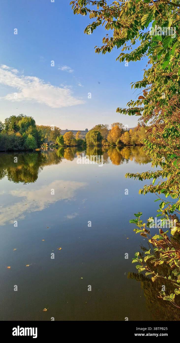 Tranquillo paesaggio autunnale con lago calmo, alberi colorati e cielo limpido che si riflette nell'acqua ferma. Foto Stock