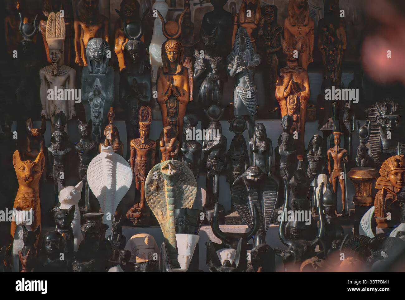 Assortimento di statue di souvenir egiziani tra cui faraoni, dei, dee, cobra e gatti, ben disposti e illuminati con un'illuminazione spettacolare Foto Stock