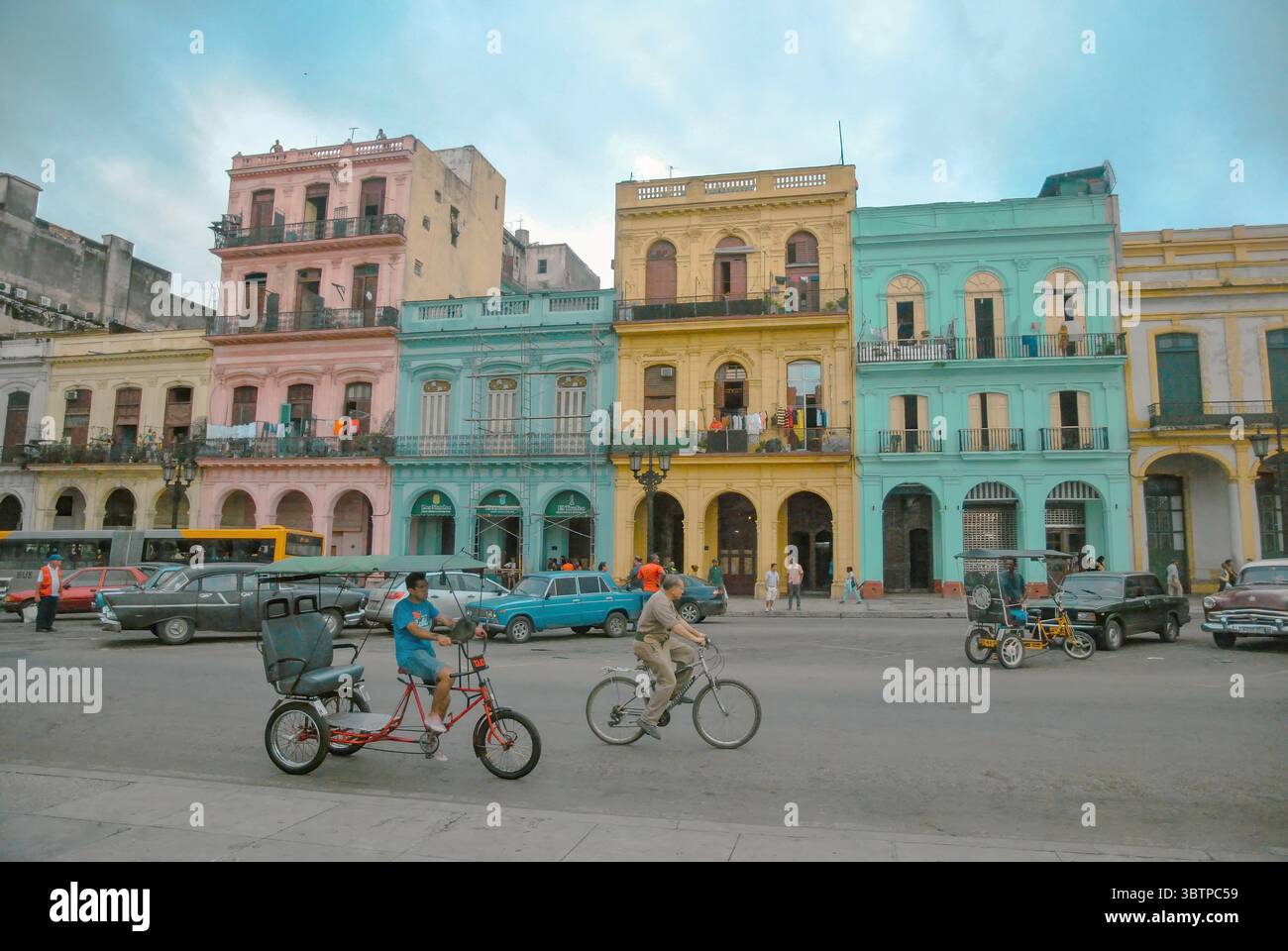 Colorati edifici coloniali nel centro di l'Avana, Cuba. Persone, biciclette e auto d'epoca di fronte alle facciate color pastello su una vivace strada cittadina. Foto Stock