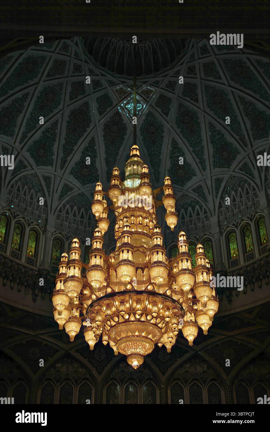 Lussuoso lampadario sospeso da un soffitto a cupola riccamente decorato in una moschea. Interni islamici decorati con dettagli in vetro colorato. Foto Stock