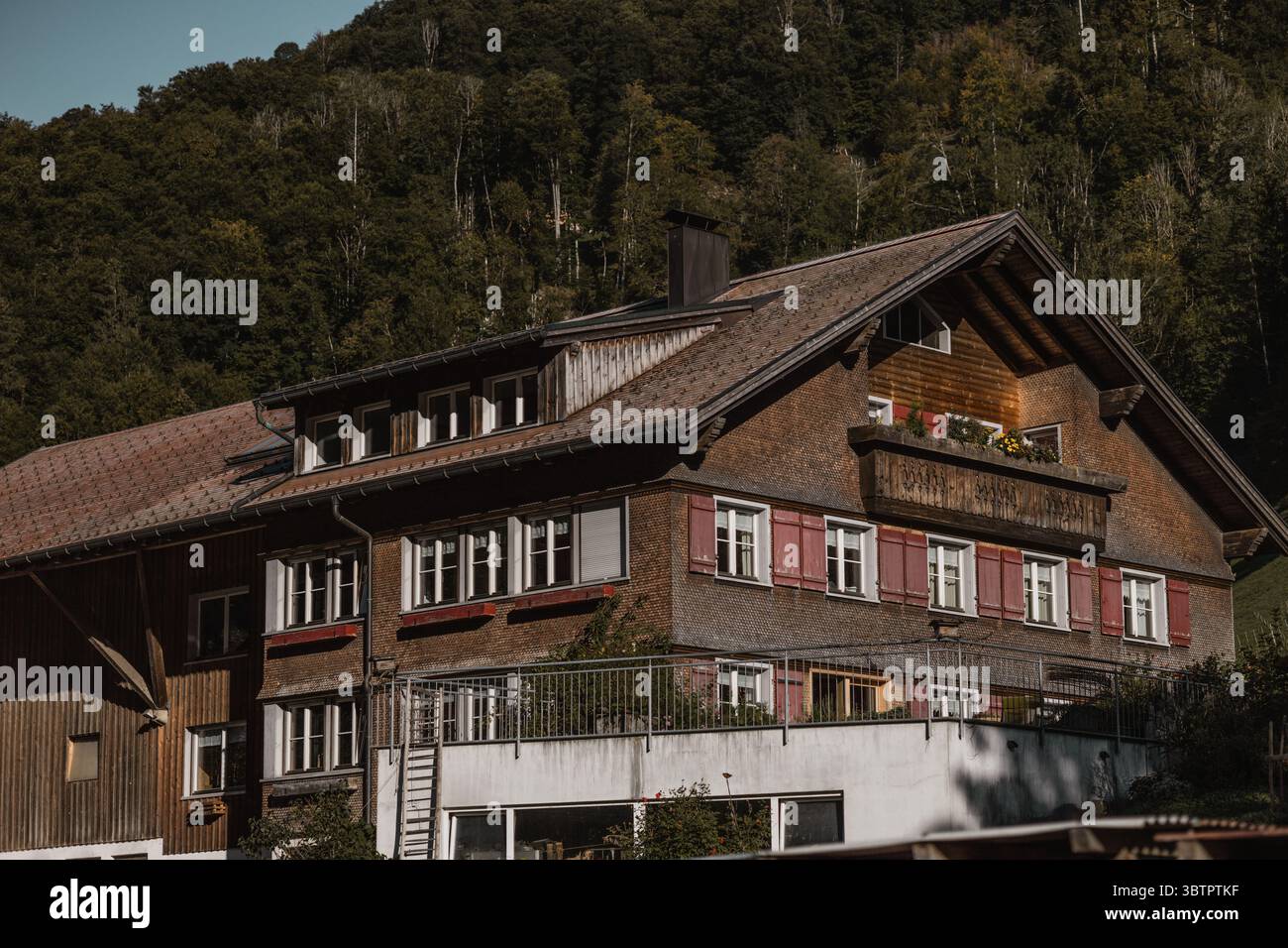 Una vecchia grande casa colonica con una facciata in legno e persiane rosse, un balcone e una finestra dormitorio Foto Stock