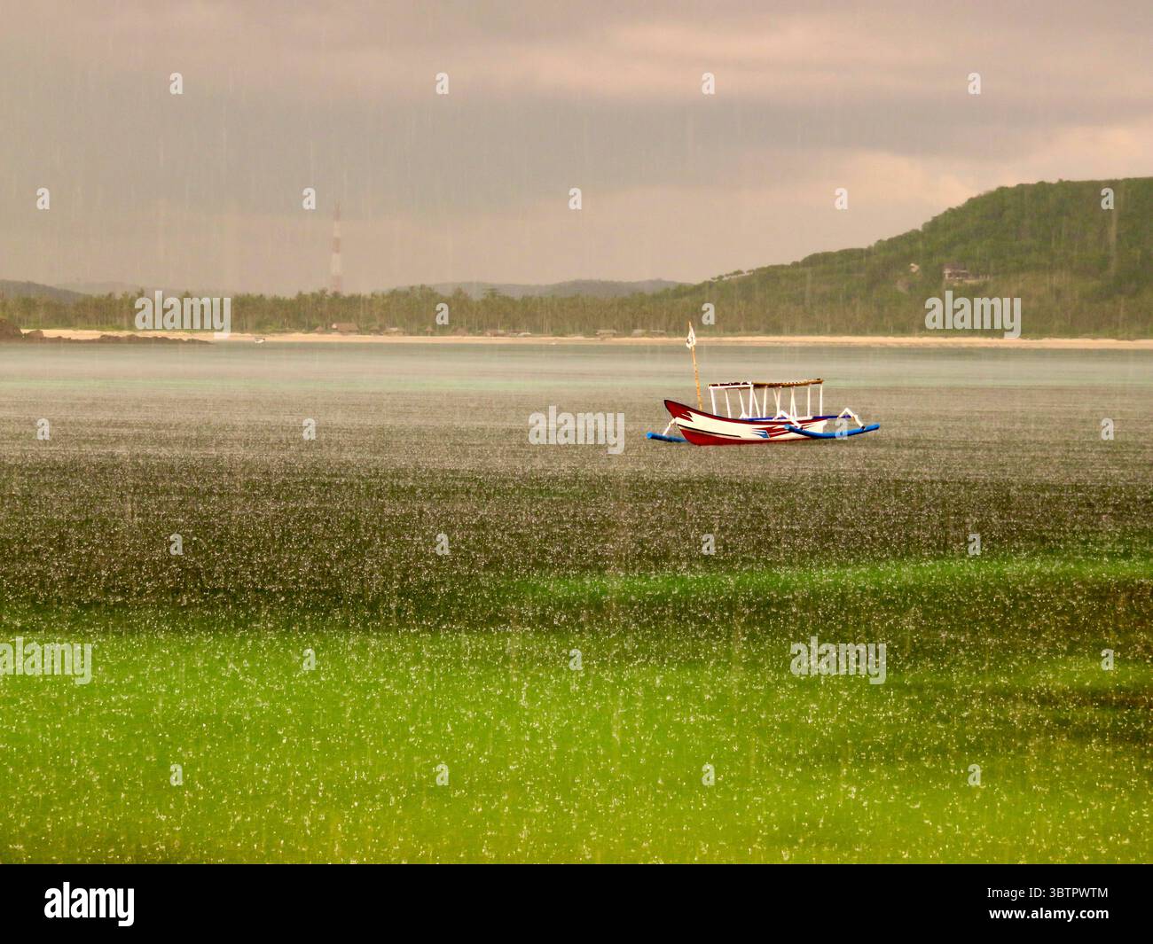 La barca tradizionale galleggia sulla superficie dell'oceano piovoso vicino a Lombok, Indonesia, con una costa nebbiosa sullo sfondo Foto Stock