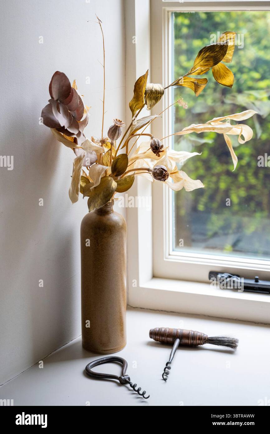 Fiori secchi con teste di semi e un'esposizione di cavatappi vicino a una finestra di cottage in Inghilterra Foto Stock