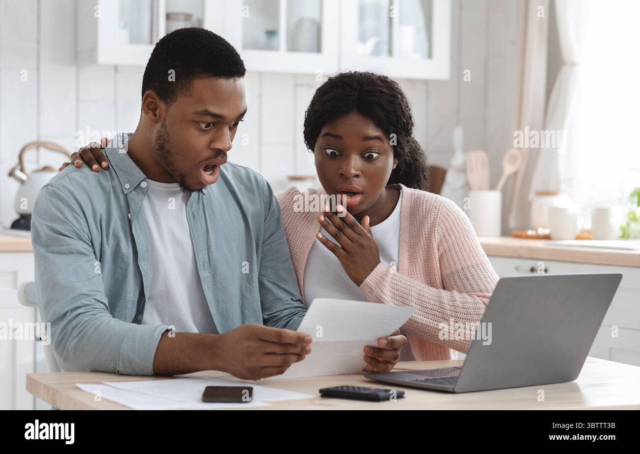 Scioccato coppia nera in cucina che ha problemi finanziari, facendo calcoli di bilancio di famiglia Foto Stock