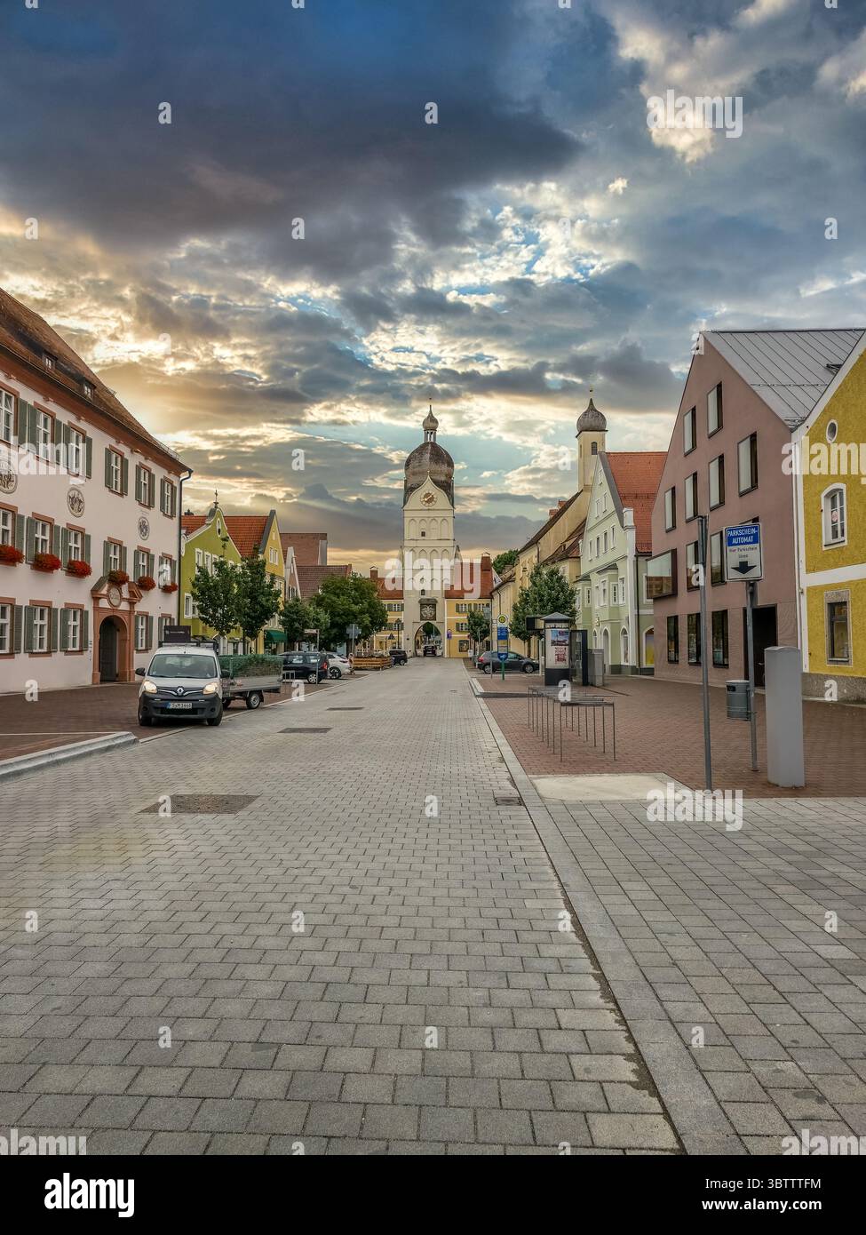 Vista della strada principale con case storiche, la splendida torre ex porta della città di Erding, Germania, con il suggestivo cielo del tramonto Foto Stock
