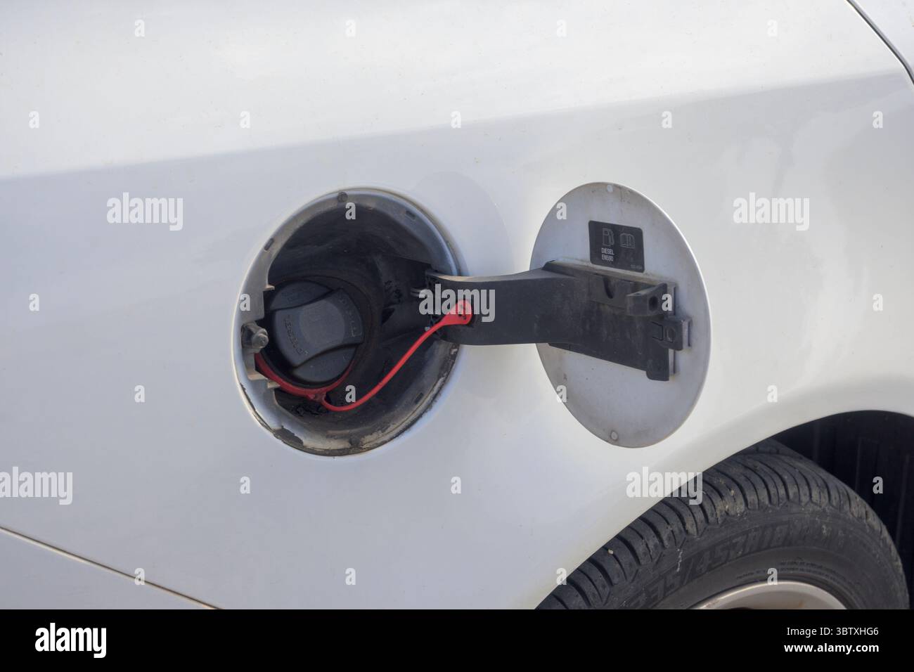 Primo piano di un tappo aperto del serbatoio del carburante su una vettura bianca, con l'etichetta del diesel e il tappo protettivo con una cinghia di fissaggio rossa. L'immagine si concentra su Foto Stock