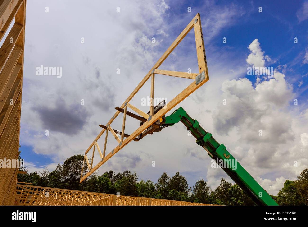 Lavoratori qualificati impiegano gru per posizionare capriate in legno per progetti di nuova costruzione in un'area industriale. Foto Stock